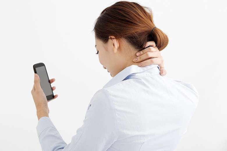 woman holding her neck from pain looking at smartphone