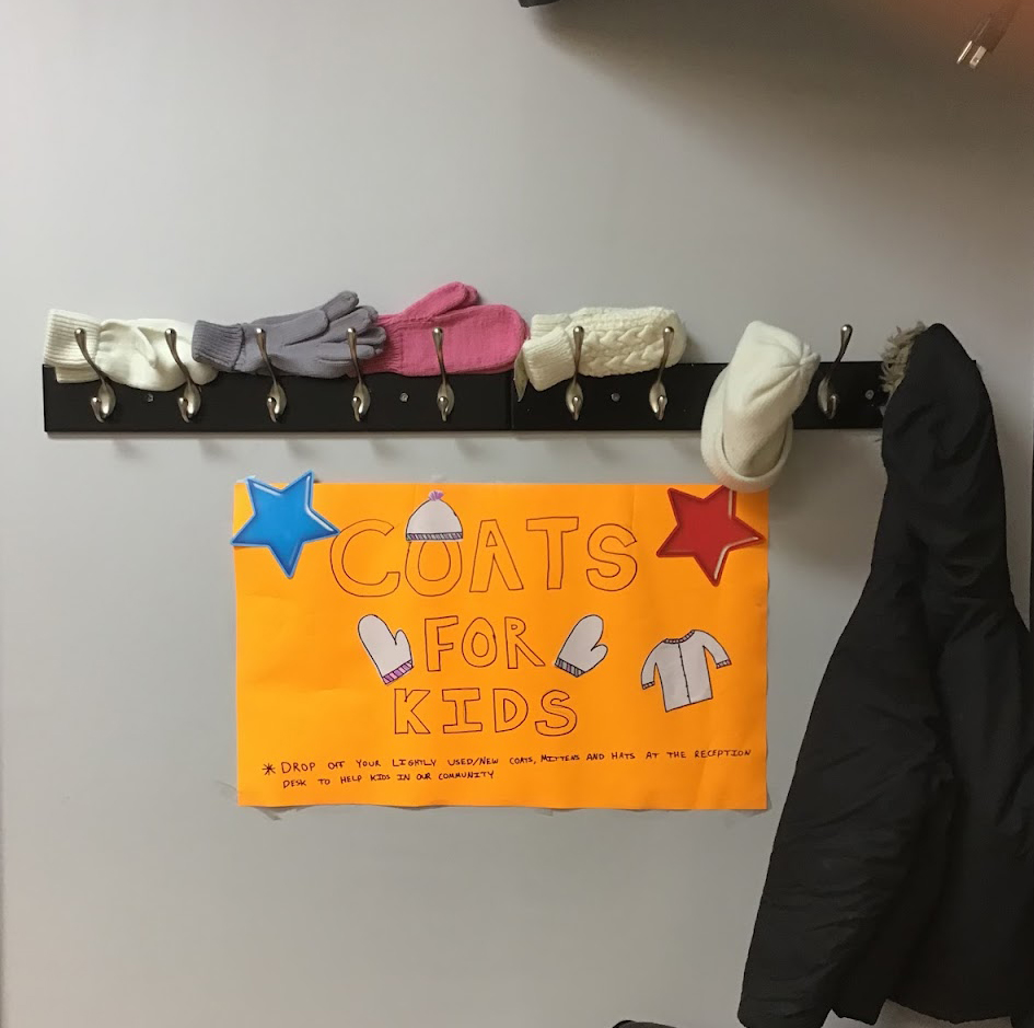 jackets and mittens hanging on a coat hanger with a yellow coats for kids sign on the wall