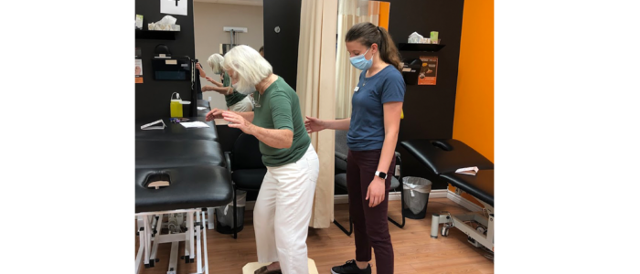 physiotherapy assistant helps elderly patient balance on board