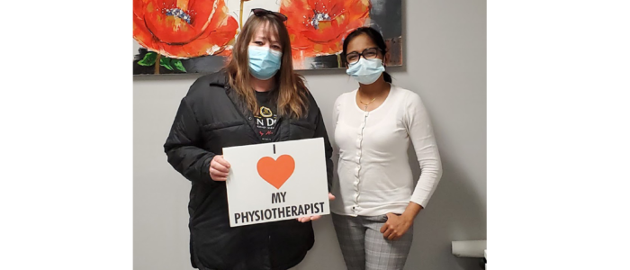 physiotherapist stands side by side with recovered patient holding a I love physiotherapist sign